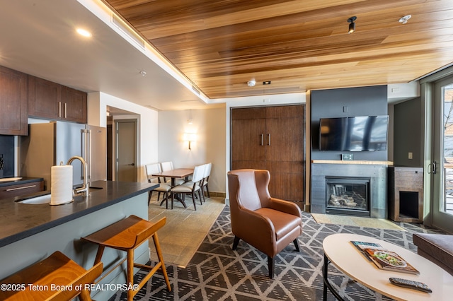 living room featuring a tiled fireplace, sink, and wooden ceiling