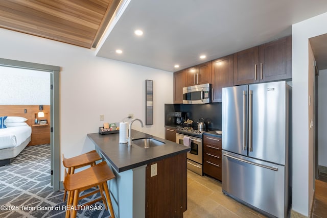 kitchen featuring sink, dark brown cabinets, stainless steel appliances, a kitchen breakfast bar, and kitchen peninsula