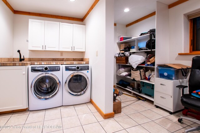 clothes washing area with light tile patterned floors, washer and clothes dryer, a sink, and cabinet space