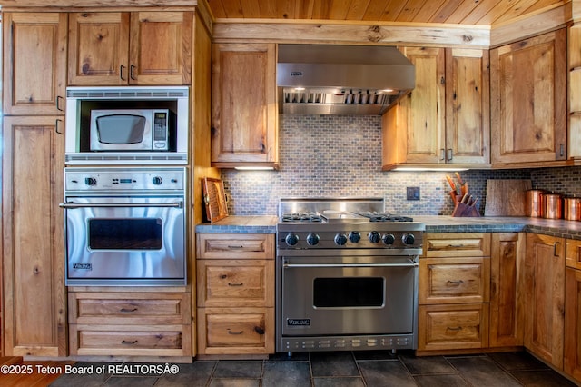 kitchen featuring appliances with stainless steel finishes, brown cabinets, wall chimney range hood, and tasteful backsplash