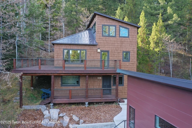 rear view of house featuring a deck, metal roof, a standing seam roof, and a wooded view