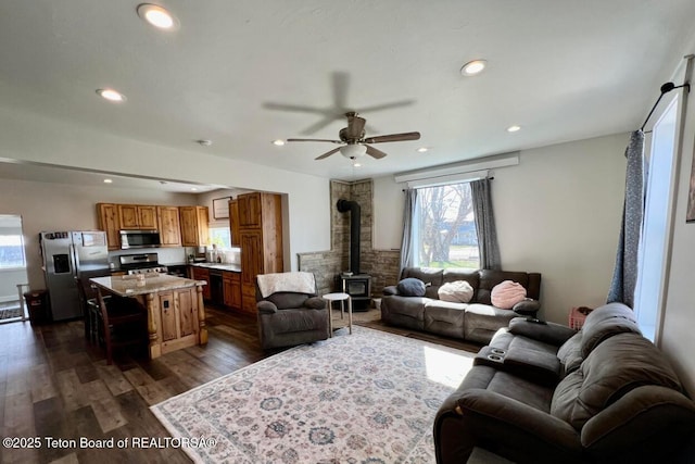 living room with dark wood-type flooring, ceiling fan, and a wood stove