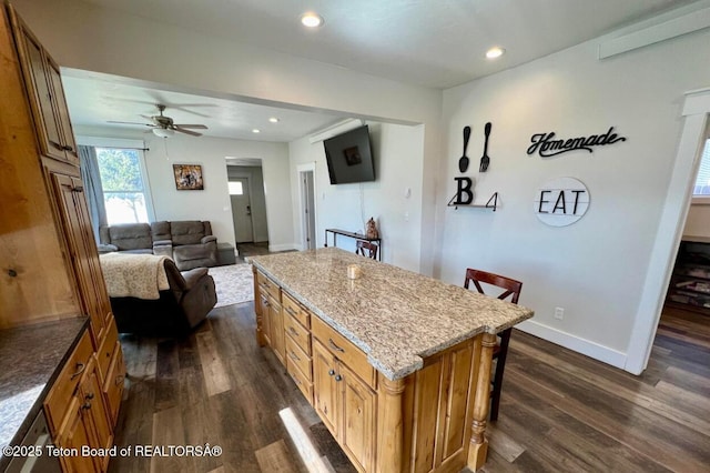 kitchen featuring dark wood-type flooring, a breakfast bar, light stone counters, a center island, and ceiling fan