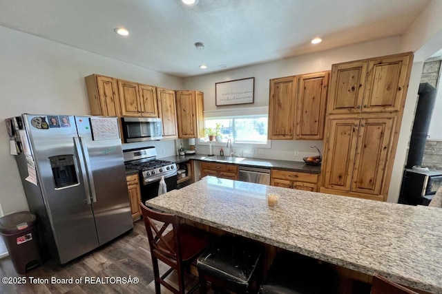 kitchen featuring sink, a kitchen breakfast bar, stainless steel appliances, dark hardwood / wood-style floors, and light stone counters