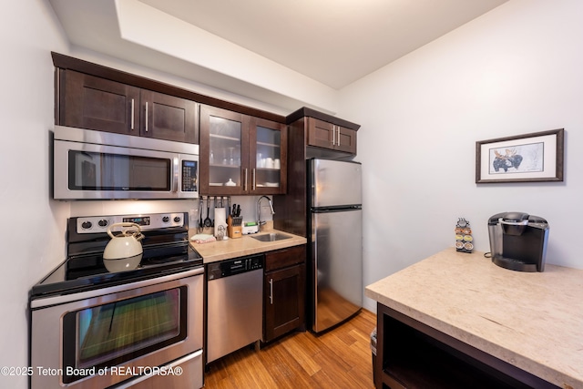 kitchen with stainless steel appliances, sink, dark brown cabinets, and light hardwood / wood-style flooring