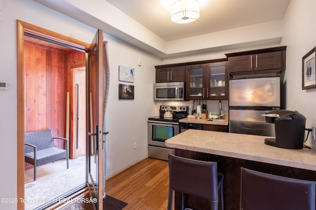 kitchen featuring dark brown cabinetry, a kitchen breakfast bar, stainless steel appliances, and light hardwood / wood-style floors