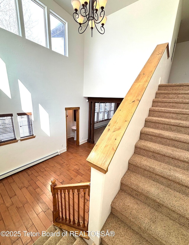 staircase featuring hardwood / wood-style floors, baseboards, a baseboard radiator, an inviting chandelier, and a high ceiling