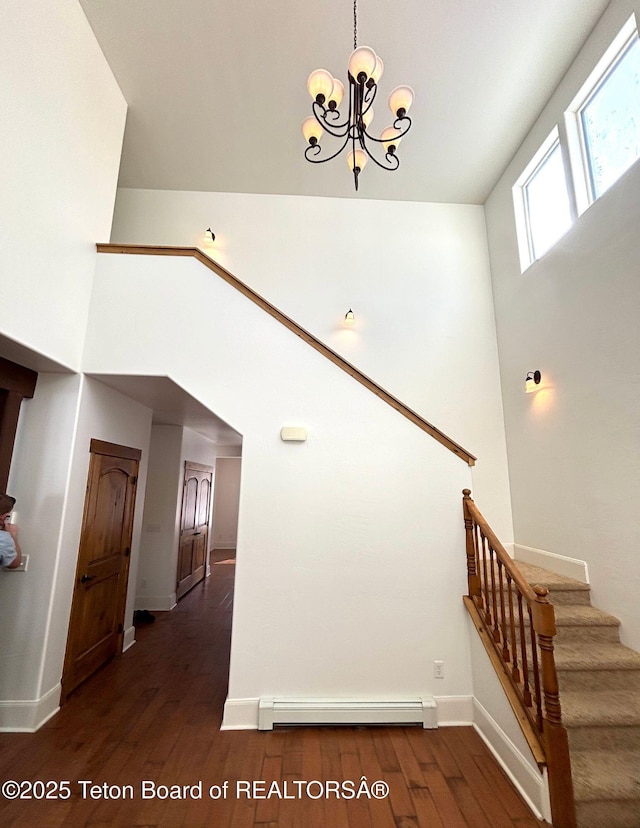 stairs with wood finished floors, a towering ceiling, and a baseboard radiator