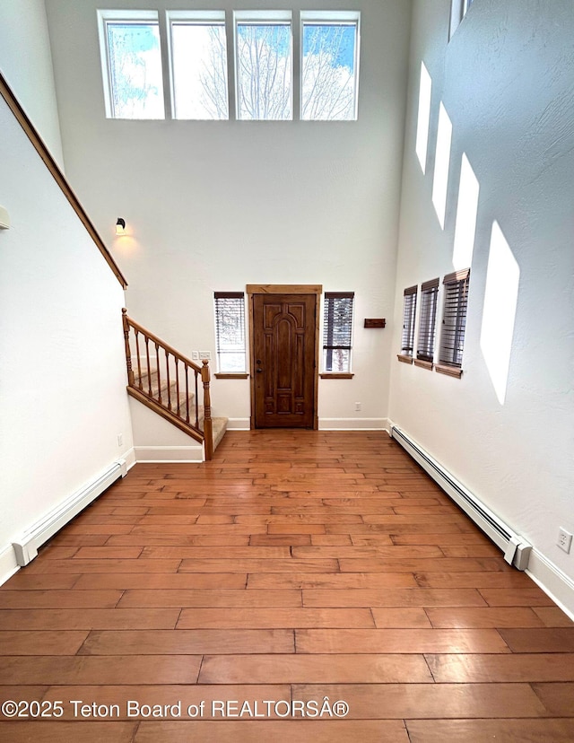 entryway with baseboard heating, stairway, a high ceiling, and wood-type flooring