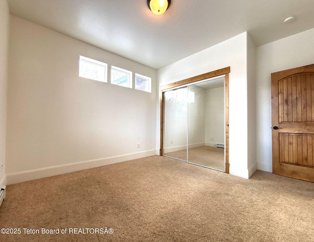 unfurnished bedroom featuring a closet, baseboard heating, baseboards, and carpet floors