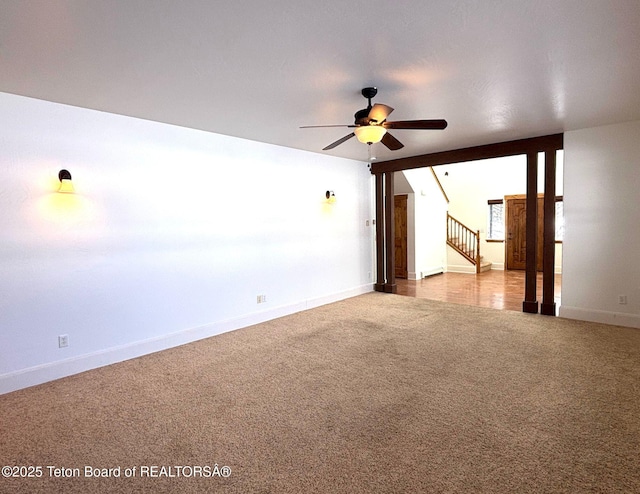 carpeted spare room featuring stairway, baseboards, and ceiling fan