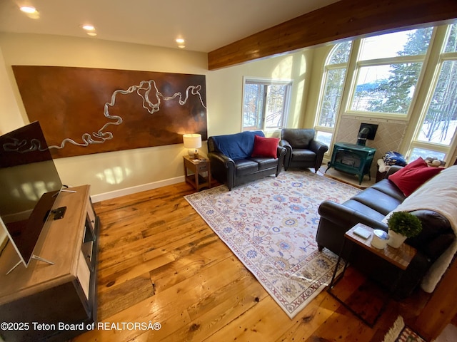 living area with baseboards, wood finished floors, beamed ceiling, a wood stove, and recessed lighting