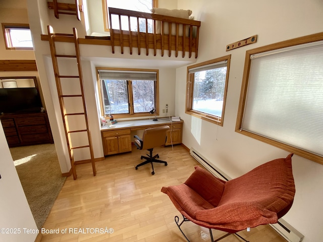 office space with a baseboard radiator, a high ceiling, built in desk, and light wood finished floors