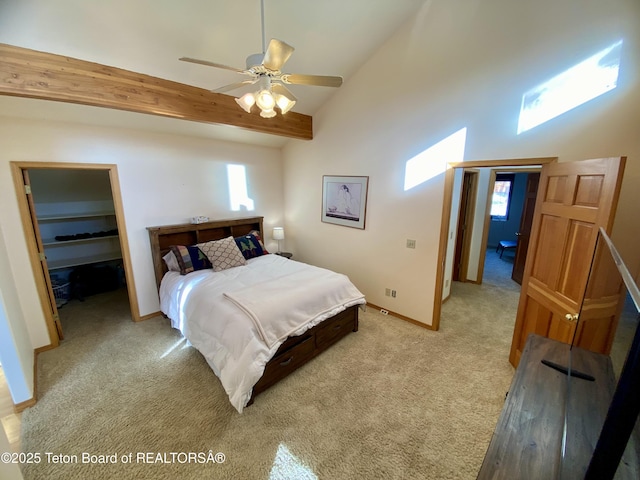 bedroom featuring light carpet, baseboards, ceiling fan, a walk in closet, and high vaulted ceiling