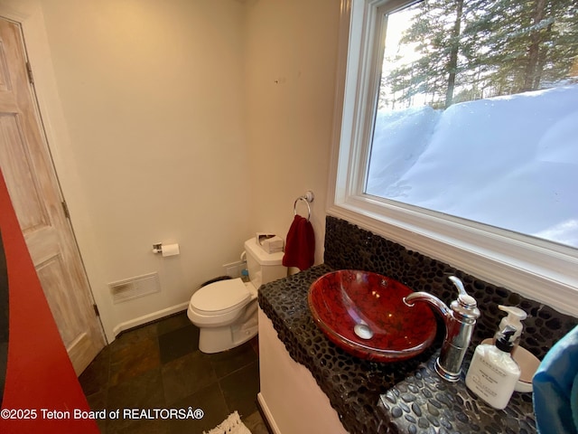 half bath with toilet, baseboards, visible vents, and a sink