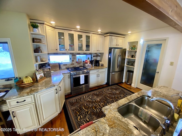 kitchen featuring white cabinets, glass insert cabinets, light stone countertops, stainless steel appliances, and a sink