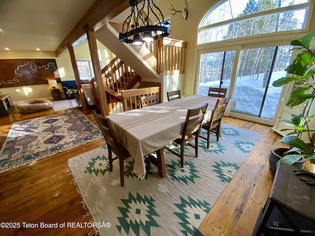 dining space with a towering ceiling, a notable chandelier, stairway, and wood finished floors