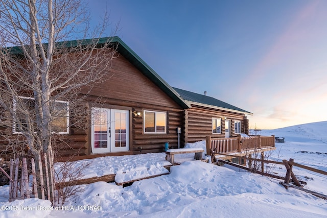 snow covered house featuring log siding and french doors