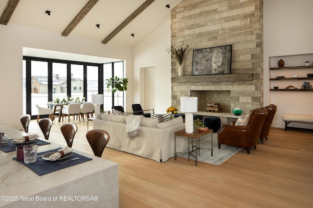 living area featuring high vaulted ceiling, wood finished floors, beam ceiling, and a stone fireplace