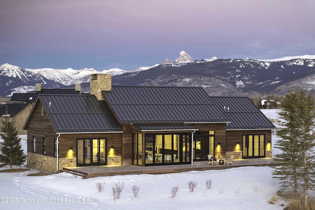 snow covered house featuring a chimney, a standing seam roof, metal roof, and a deck with mountain view