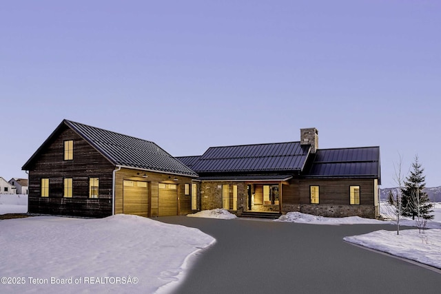 view of front facade featuring metal roof, aphalt driveway, a garage, a standing seam roof, and a chimney