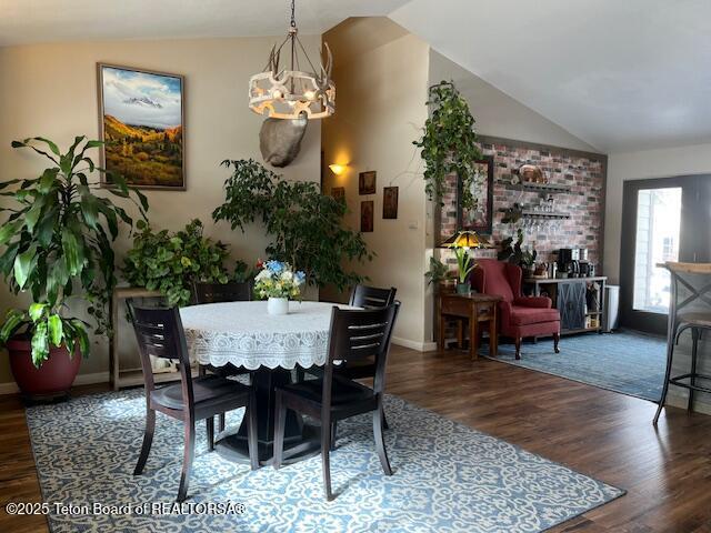 dining area with baseboards, a chandelier, vaulted ceiling, and wood finished floors