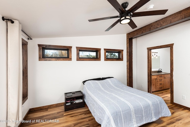 bedroom with a ceiling fan, vaulted ceiling, a sink, wood finished floors, and baseboards