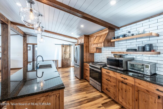 kitchen featuring a barn door, vaulted ceiling with beams, stainless steel appliances, light wood-style floors, and a sink