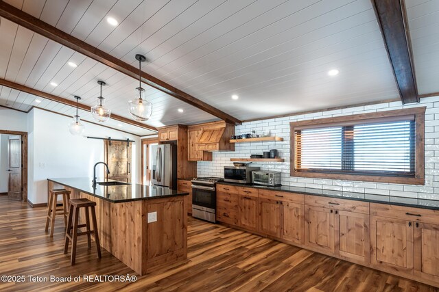 kitchen with stainless steel appliances, dark countertops, decorative backsplash, a barn door, and a sink