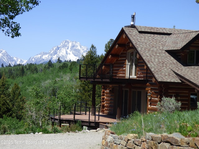 view of home's exterior with a shingled roof, a deck with mountain view, and log exterior