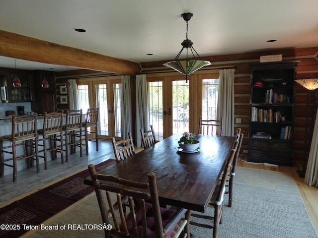 dining space featuring rustic walls, beamed ceiling, wood finished floors, and french doors