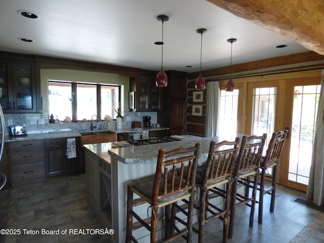 kitchen featuring a sink, backsplash, a center island, a kitchen bar, and glass insert cabinets