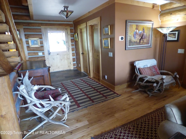 foyer featuring baseboards, log walls, and wood finished floors