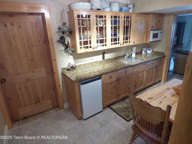 kitchen with white microwave, a sink, fridge, light stone countertops, and glass insert cabinets