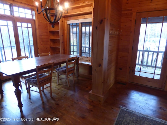 dining area with a healthy amount of sunlight, wood-type flooring, wooden walls, and a notable chandelier