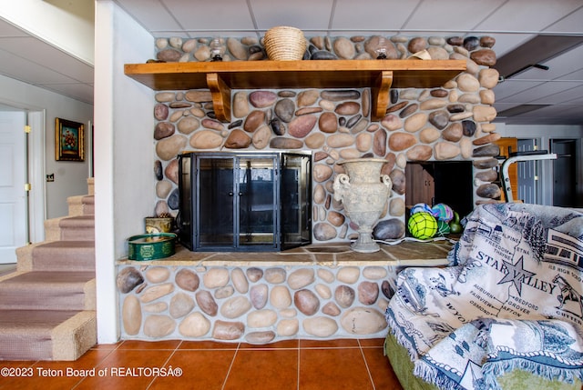 tiled living area featuring stairs, a stone fireplace, and a paneled ceiling