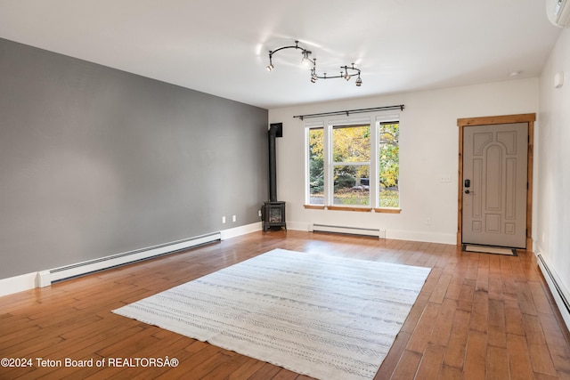 unfurnished living room featuring a baseboard heating unit, wood-type flooring, a wood stove, and baseboard heating