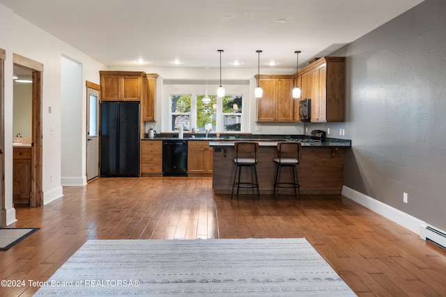 kitchen featuring dark countertops, hardwood / wood-style flooring, decorative light fixtures, a peninsula, and black appliances