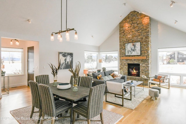 dining room with a stone fireplace, a healthy amount of sunlight, light wood finished floors, and high vaulted ceiling