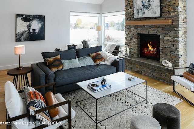 living room featuring a stone fireplace, lofted ceiling, wood finished floors, and baseboards