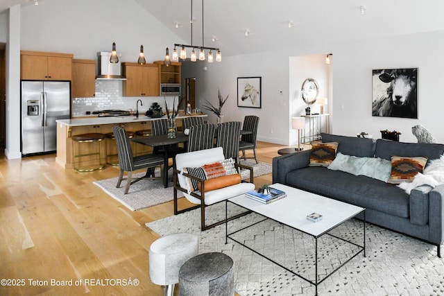 living area with light wood-style floors, baseboards, and high vaulted ceiling