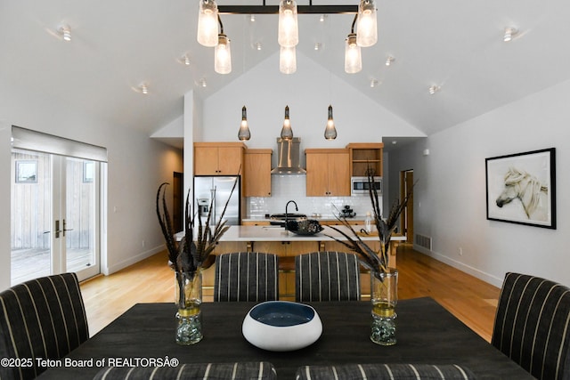 kitchen featuring light wood finished floors, tasteful backsplash, wall chimney range hood, stainless steel appliances, and open shelves