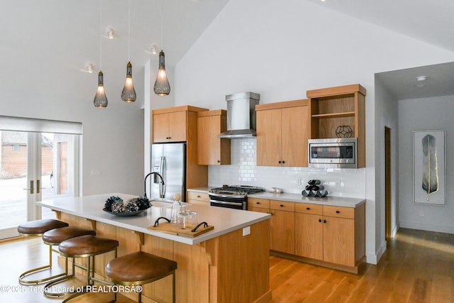 kitchen featuring open shelves, light wood-style flooring, stainless steel appliances, light countertops, and wall chimney exhaust hood