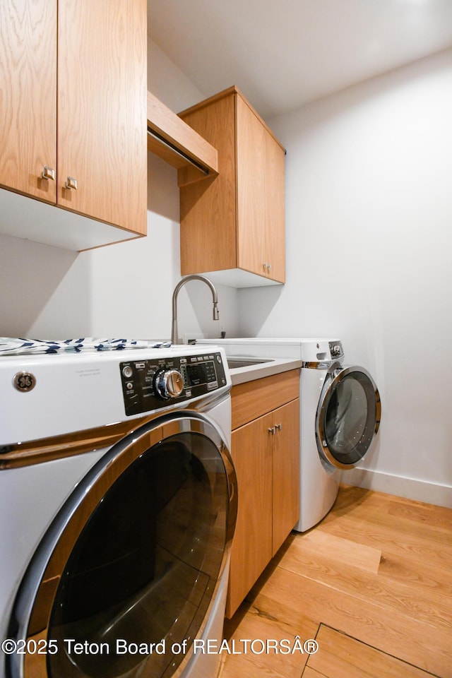 clothes washing area featuring a sink, light wood-style flooring, washer / clothes dryer, and cabinet space