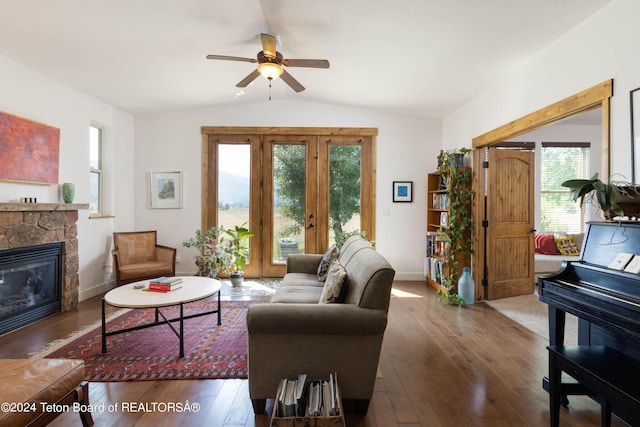 living room with lofted ceiling, wood-type flooring, baseboards, and a stone fireplace