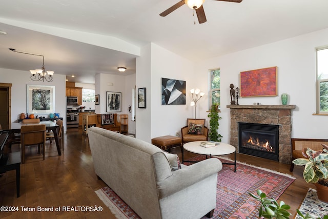 living room featuring dark wood-style floors, lofted ceiling, a stone fireplace, and ceiling fan with notable chandelier