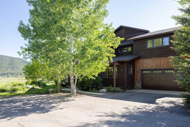 view of front facade with driveway, stone siding, an attached garage, and a mountain view