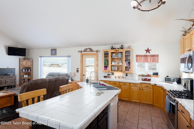 kitchen featuring tile countertops, stainless steel appliances, open floor plan, a healthy amount of sunlight, and a sink