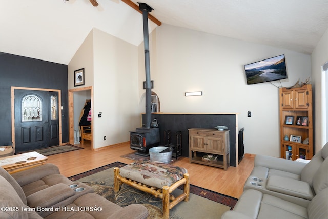 living room with beam ceiling, a ceiling fan, a wood stove, wood finished floors, and high vaulted ceiling