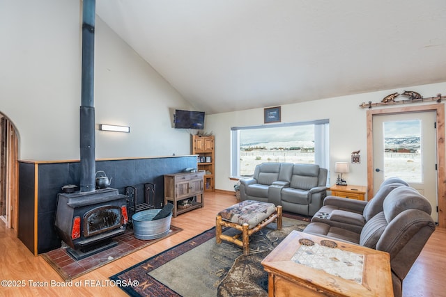 living room featuring a wood stove, light wood-style floors, and high vaulted ceiling